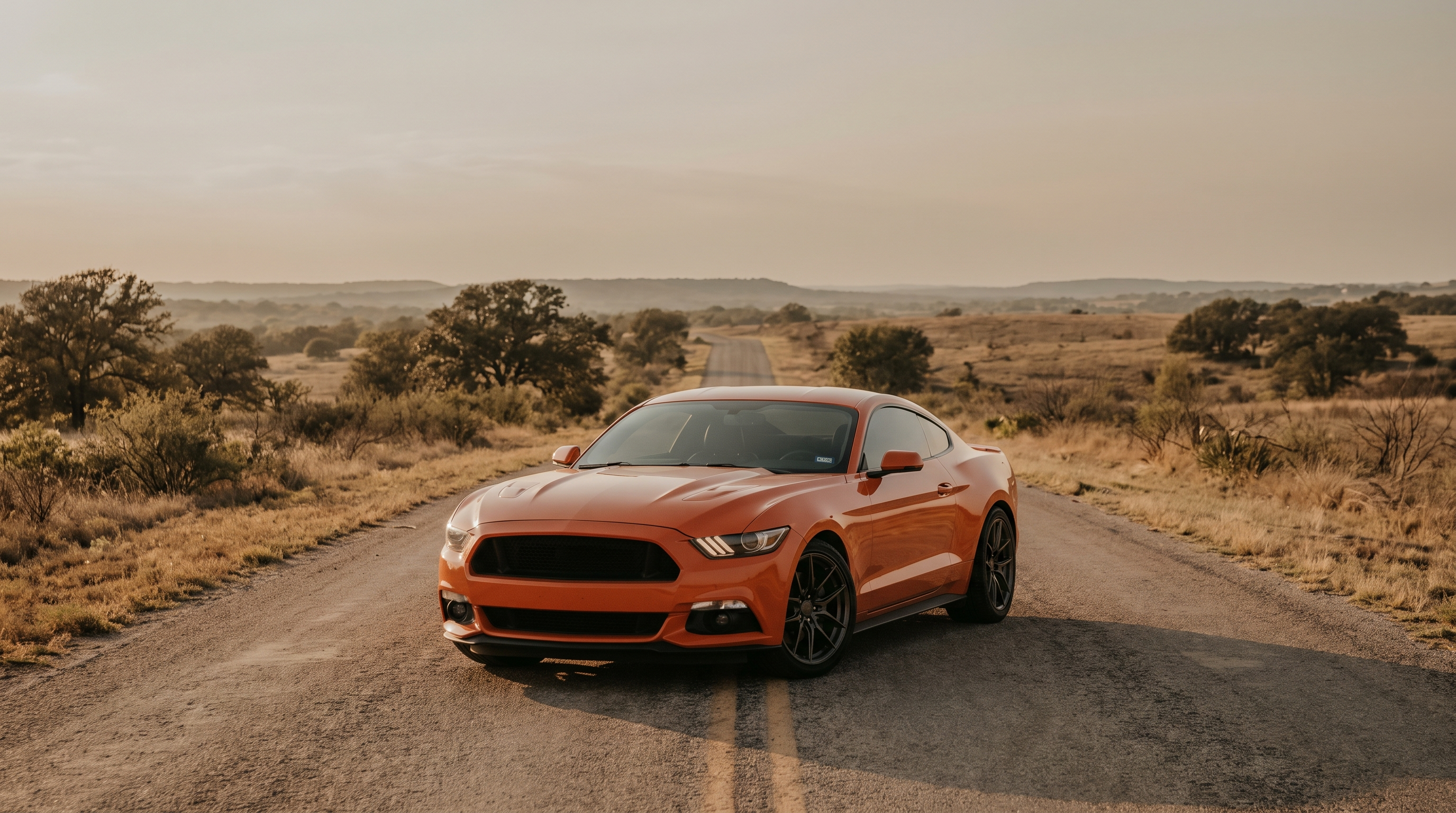 Orange 2015-2023 S550 Ford Mustang GT on an open Texas road at golden hour