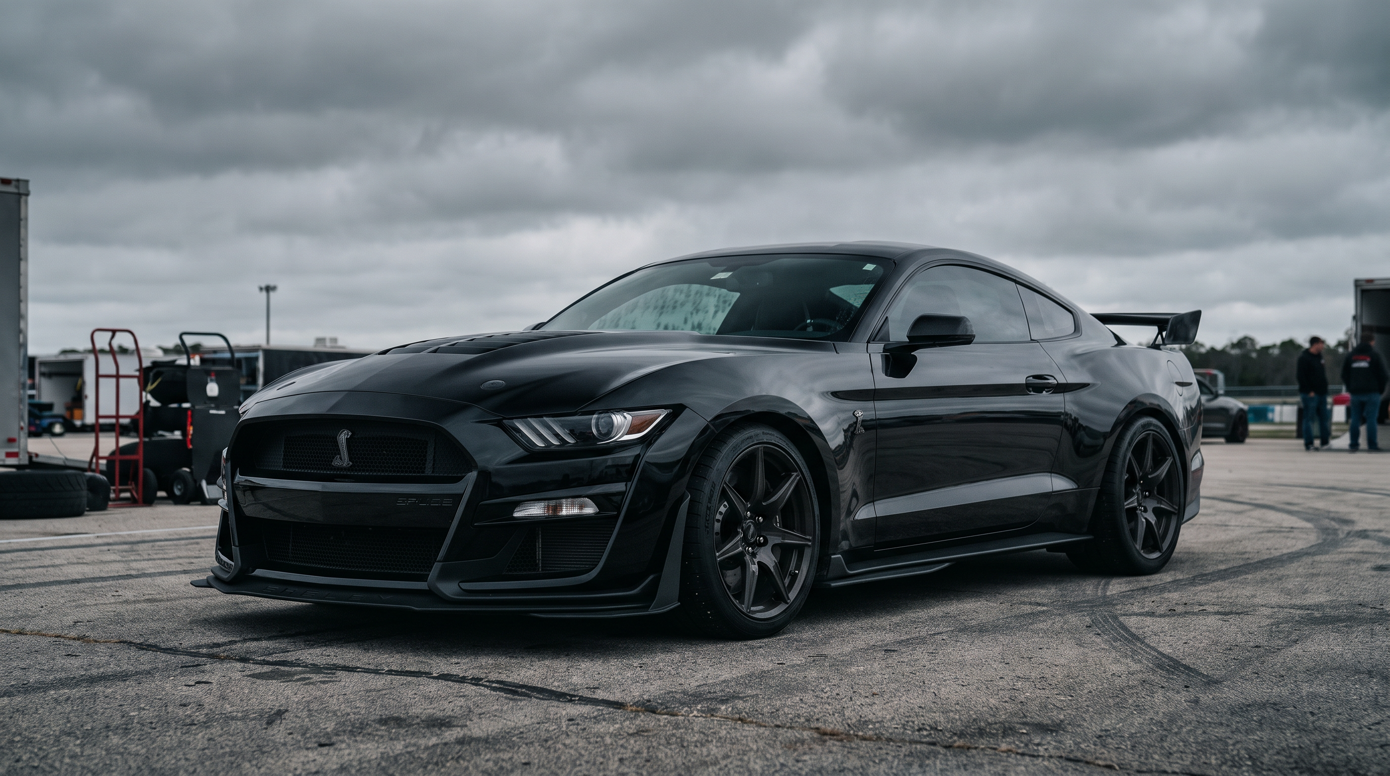 Menacing black S550-era Shelby-style Ford Mustang with aero on a race circuit paddock