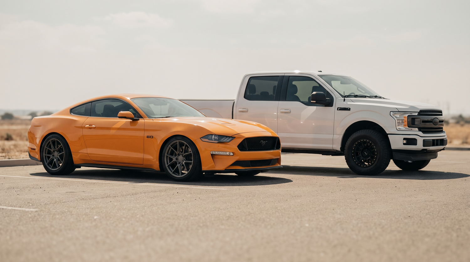 Orange Ford Mustang GT and white Ford F-150 parked showing their wheels in daylight