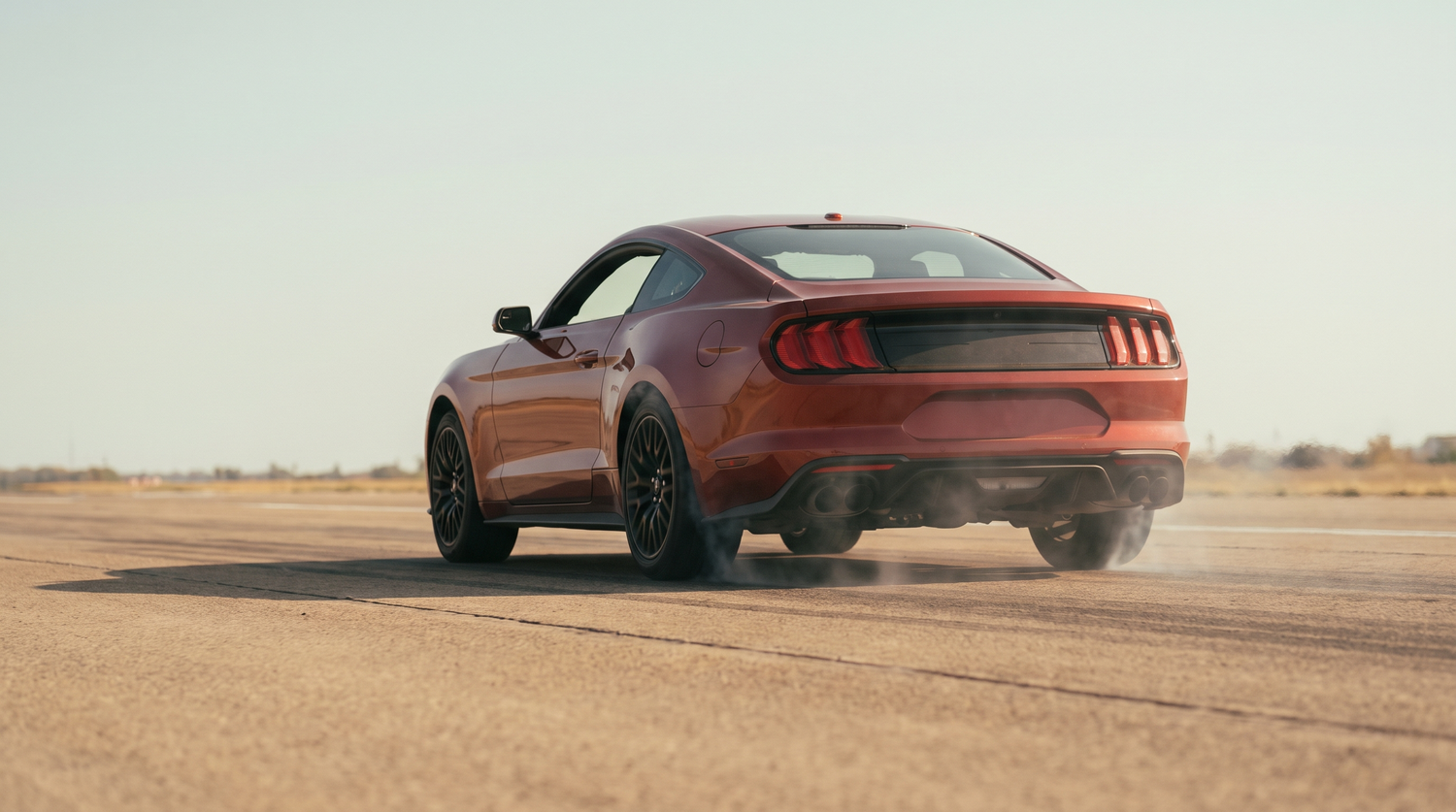 Red S550 Ford Mustang GT launching hard off the line on pavement