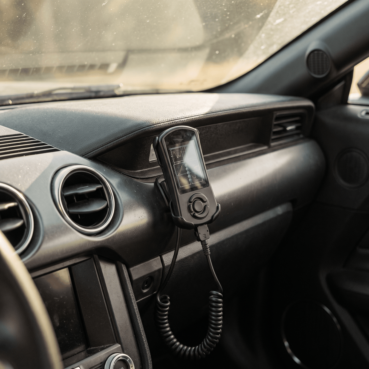 Black handheld car tuner mounted on dashboard with screen and control buttons