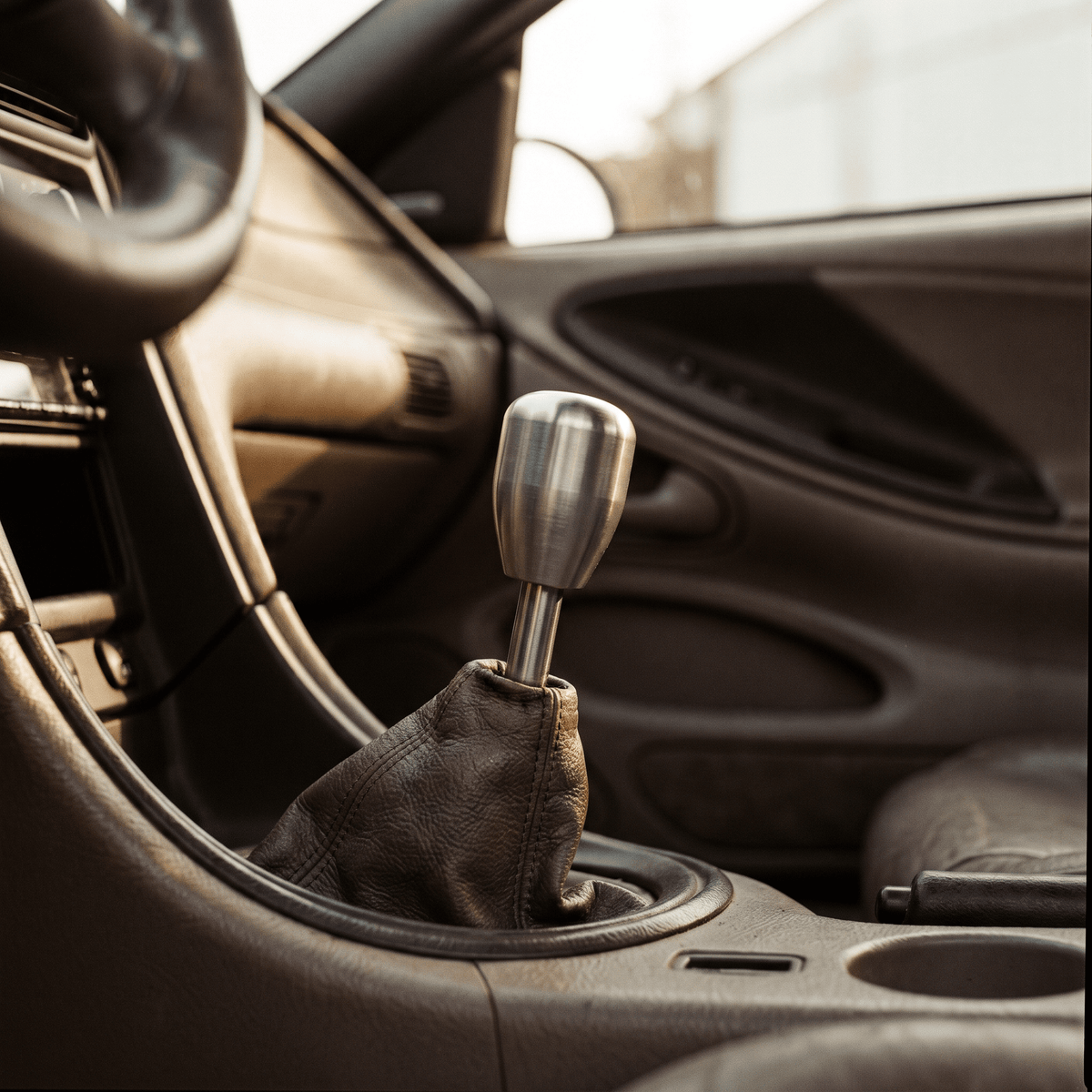 Manual gear shift with brushed stainless steel knob and dark brown leather boot in car interior
