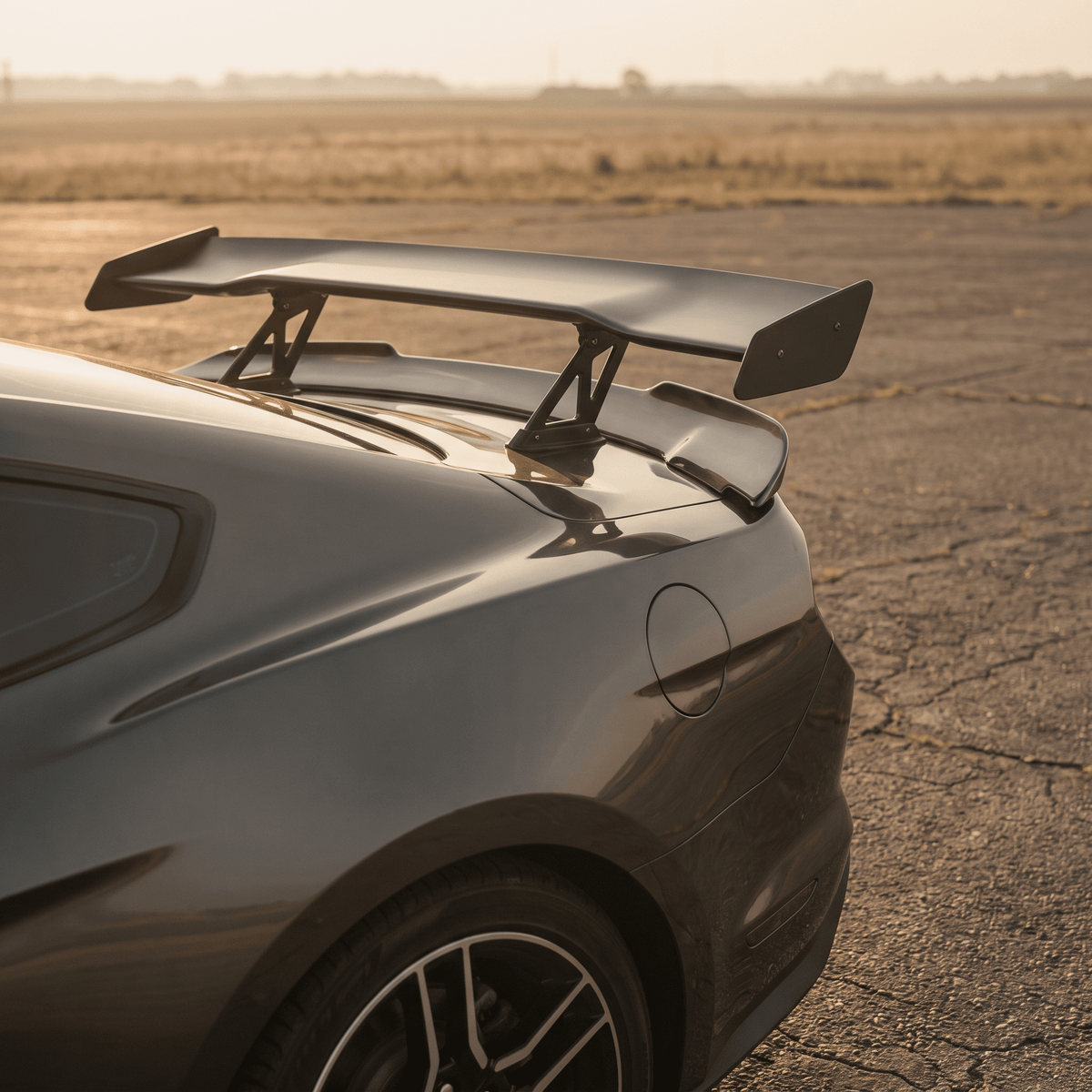 Dark metallic gray sports car with large black high-mounted racing wing and dual struts