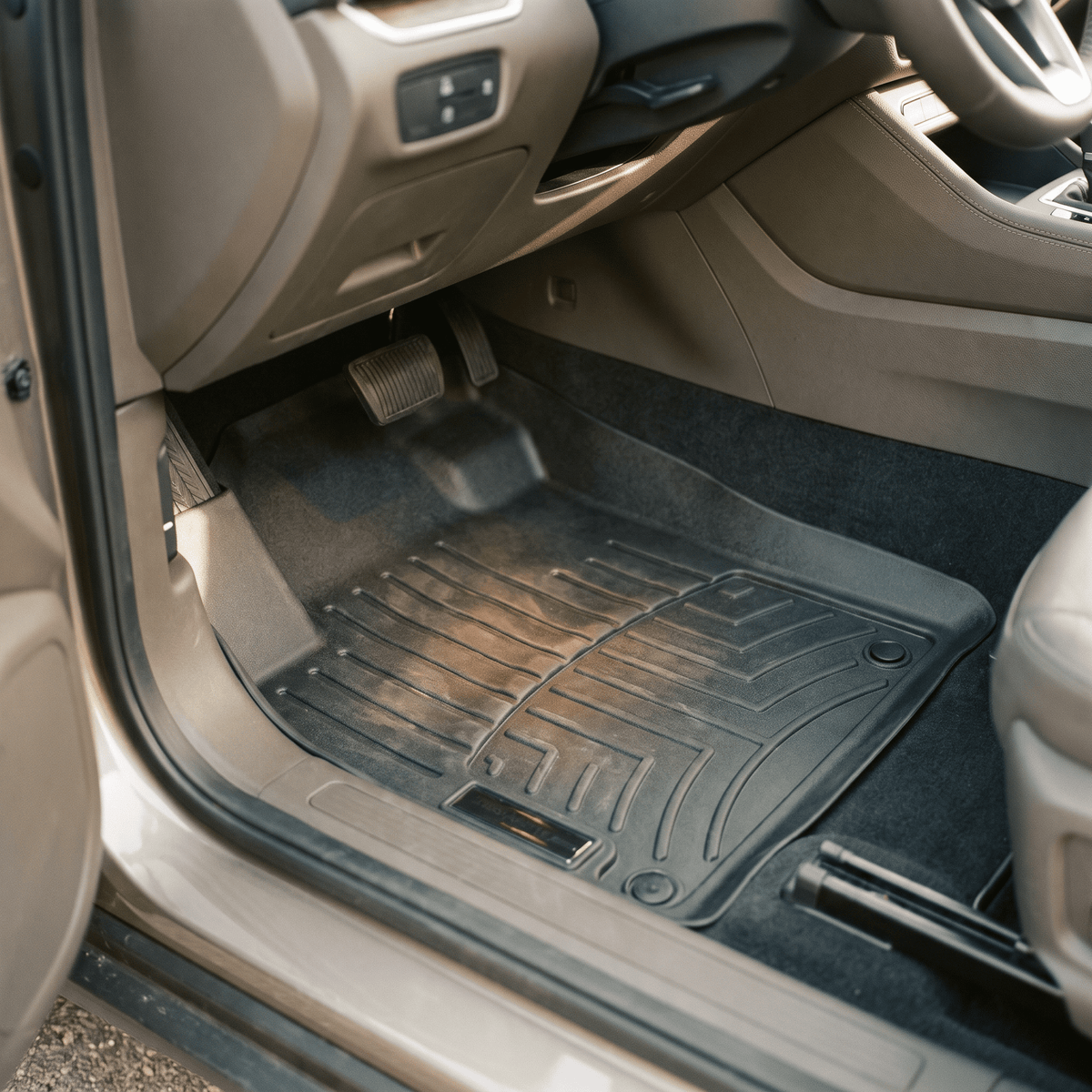 black molded rubber floor mat installed in car footwell with raised ridges and pedal cutouts