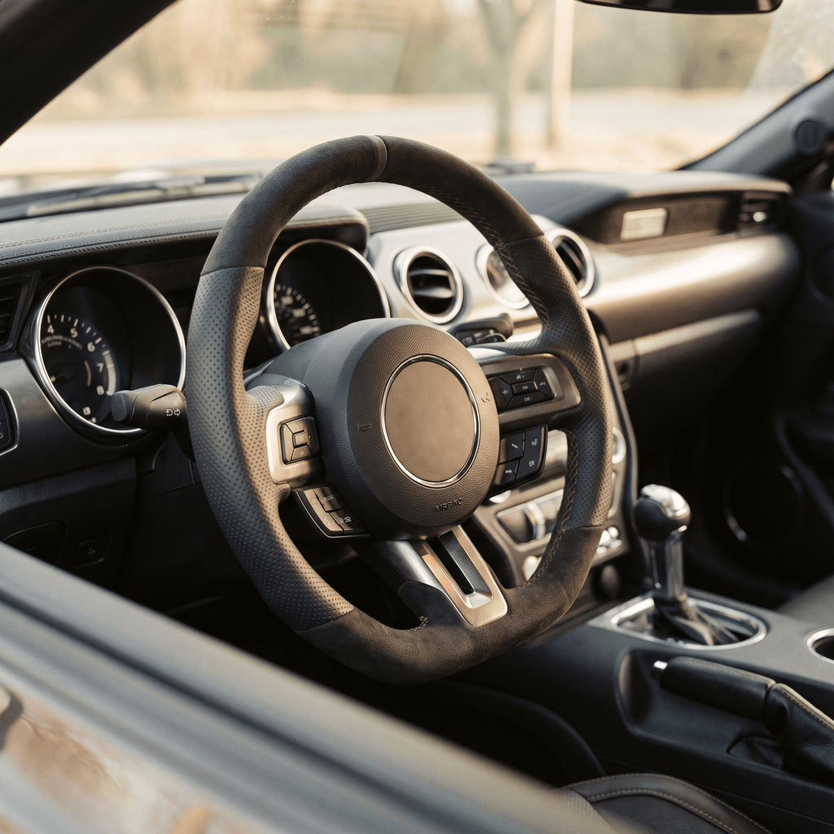 Black leather-wrapped steering wheel with perforated grip and silver multifunction buttons