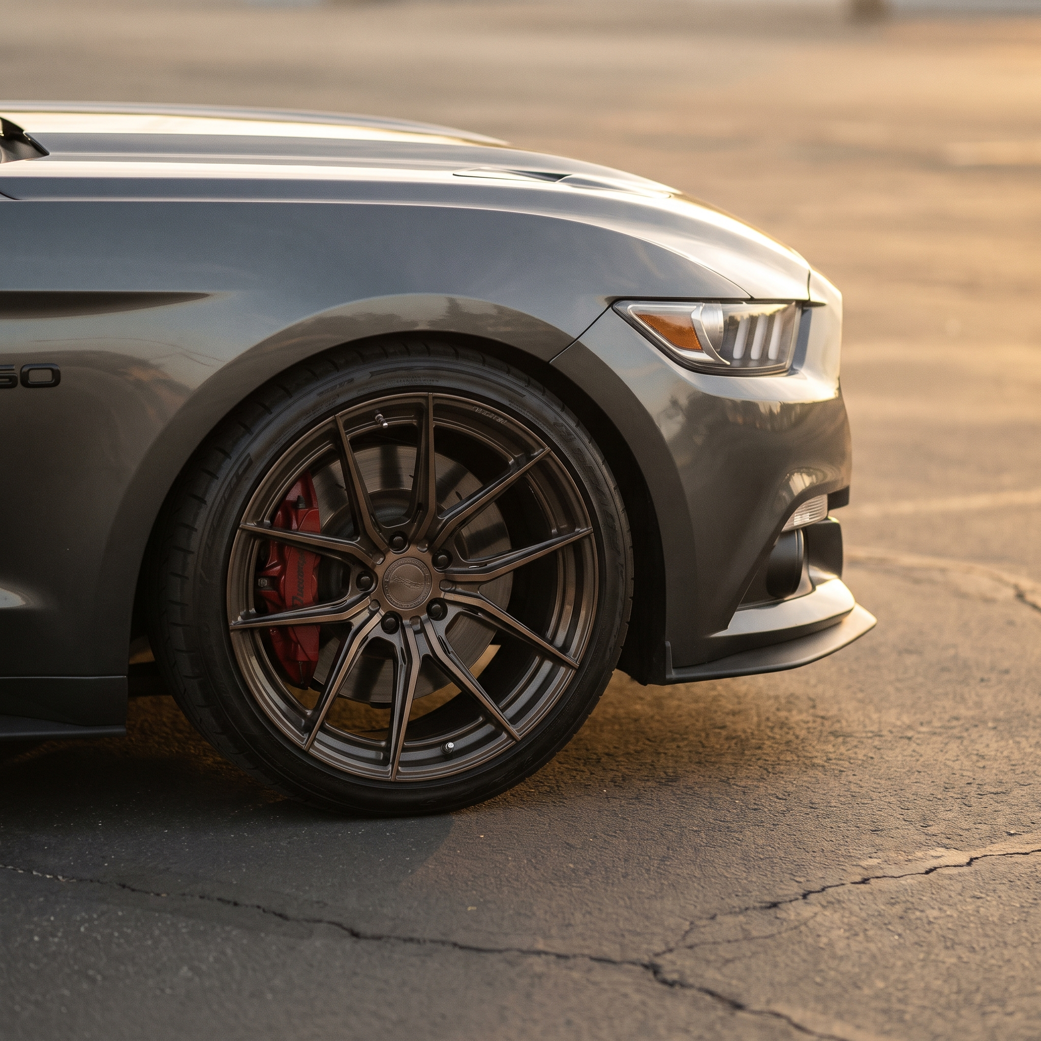 Bronze forged aftermarket wheel and red caliper on a grey Ford Mustang GT at golden hour