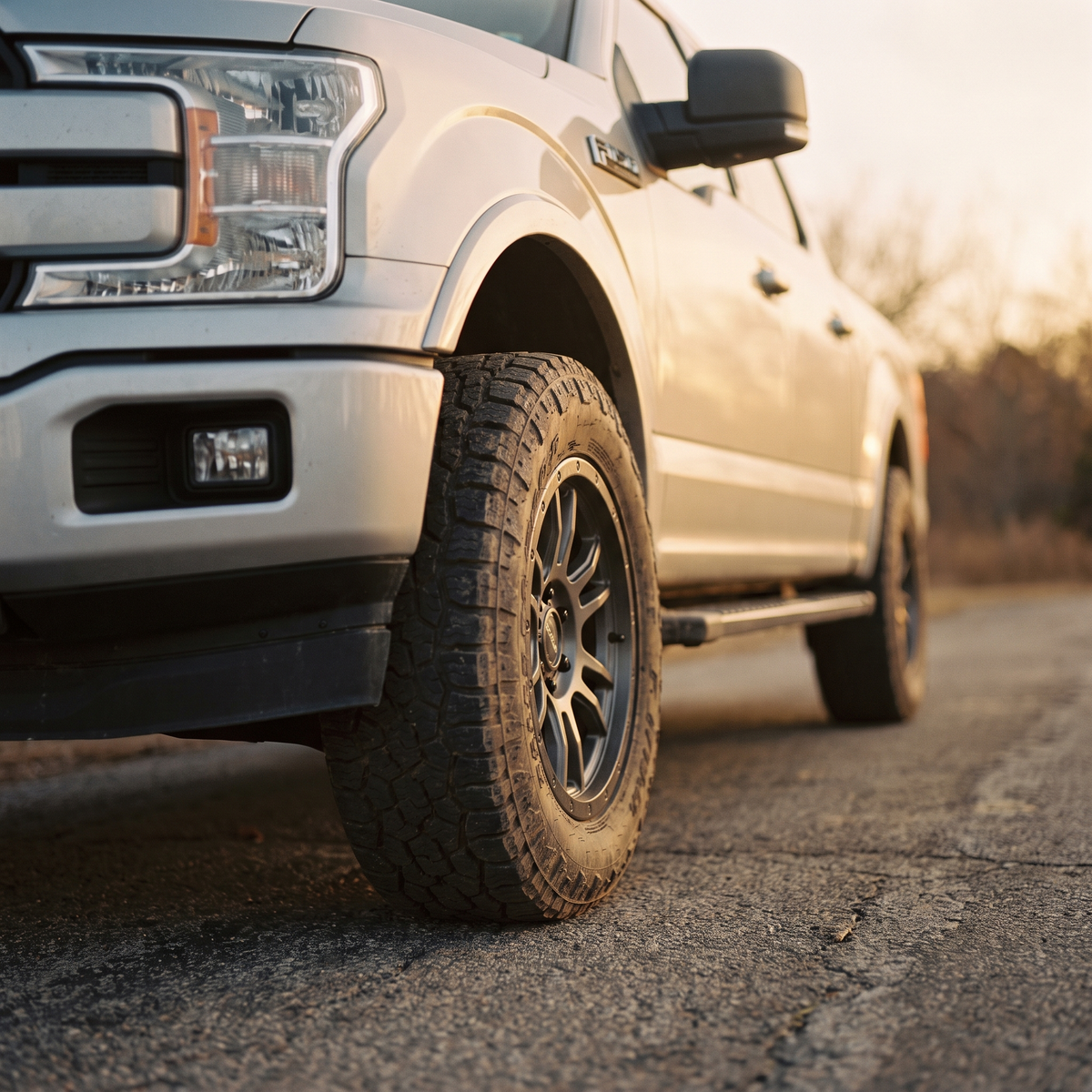 Silver 2015-2020 Ford F-150 on an aftermarket wheel and all-terrain tire at golden hour