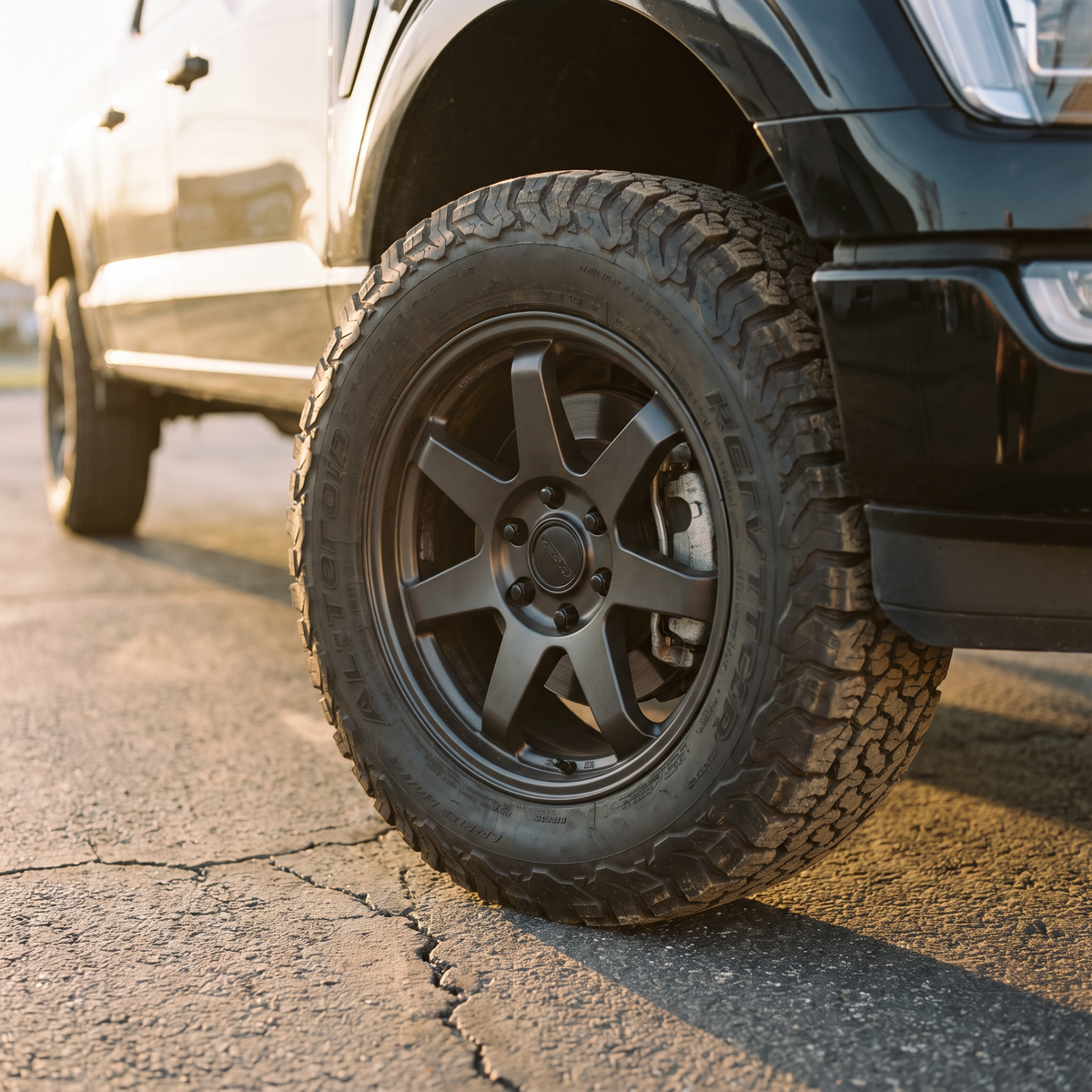 Black 2021+ Ford F-150 on an aftermarket wheel and all-terrain tire at golden hour